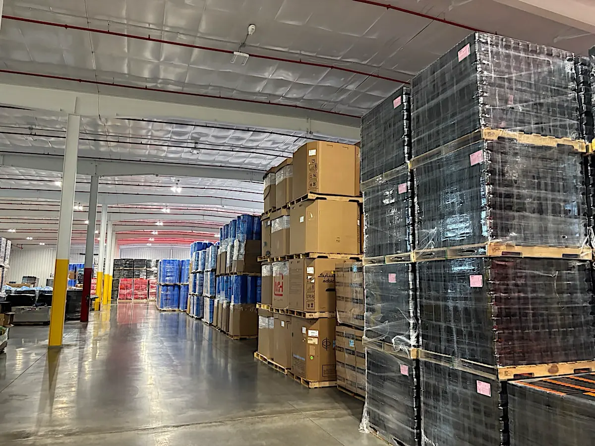 Warehouse aisle with stacked pallets of black plastic products and boxes