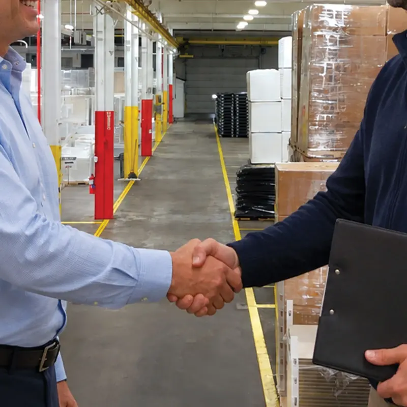 Two businesspeople shaking hands in a GHCM warehouse aisle