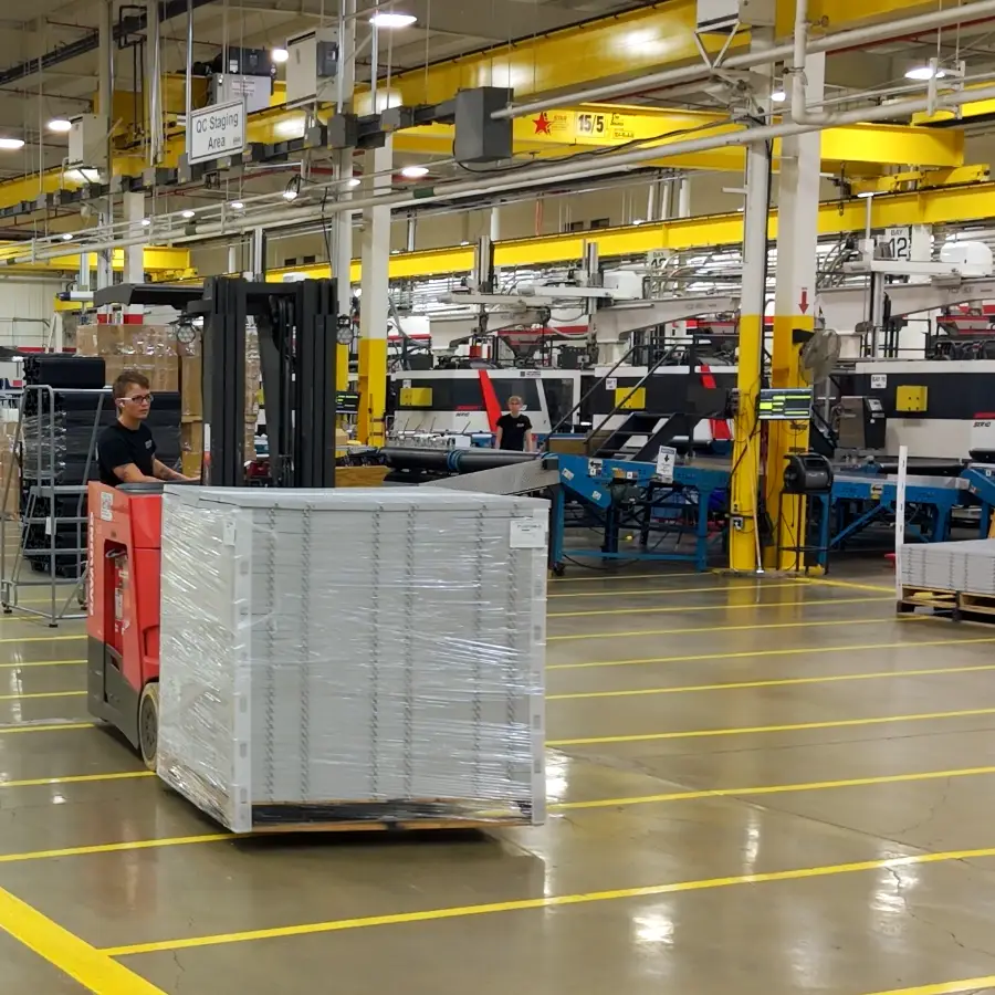 Forklift operator moving a shrink-wrapped pallet across the plant floor